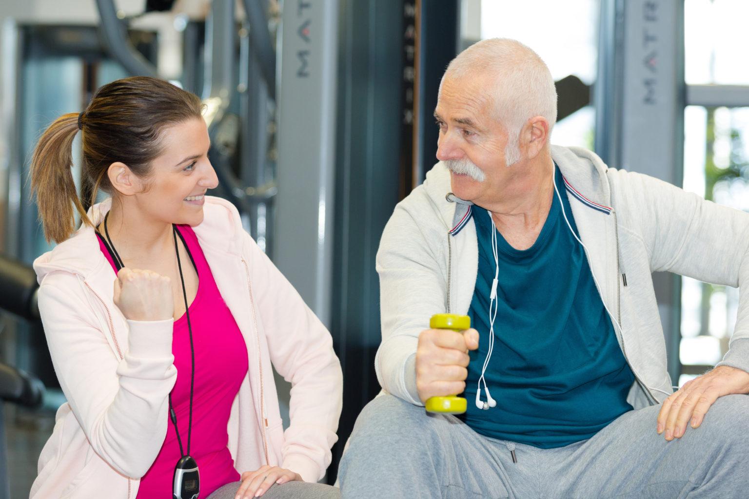 happy physiotherapist assisting senior man in lifting dumbbells